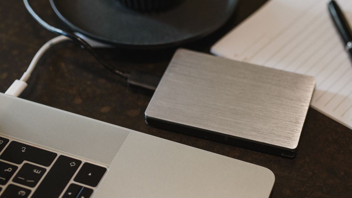 Hard disk eksternal tersambung ke laptop dengan kabel USB di atas meja kerja